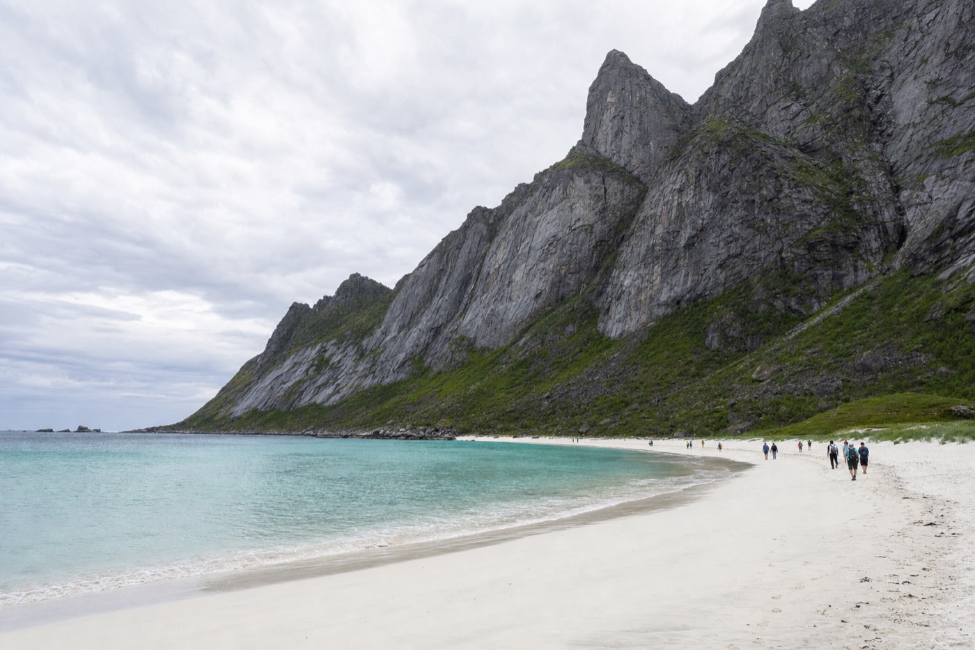 A wide white sand beach beneath sheer granite peaks with shallow turquoise water