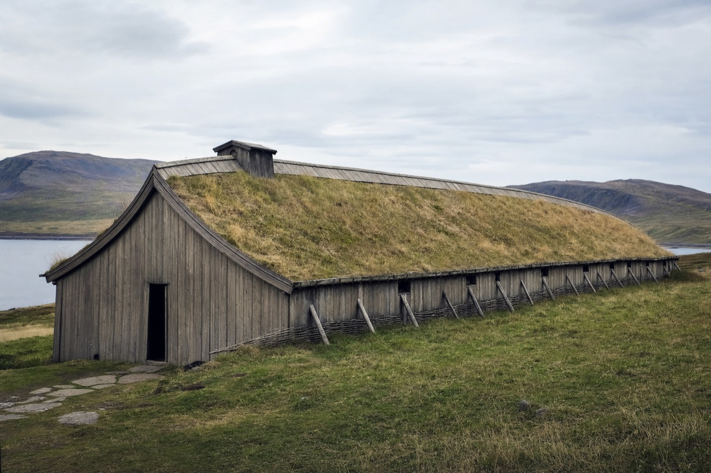 A long reconstructed Viking-age turf-roofed longhouse on an open grassy hillside in Lofoten