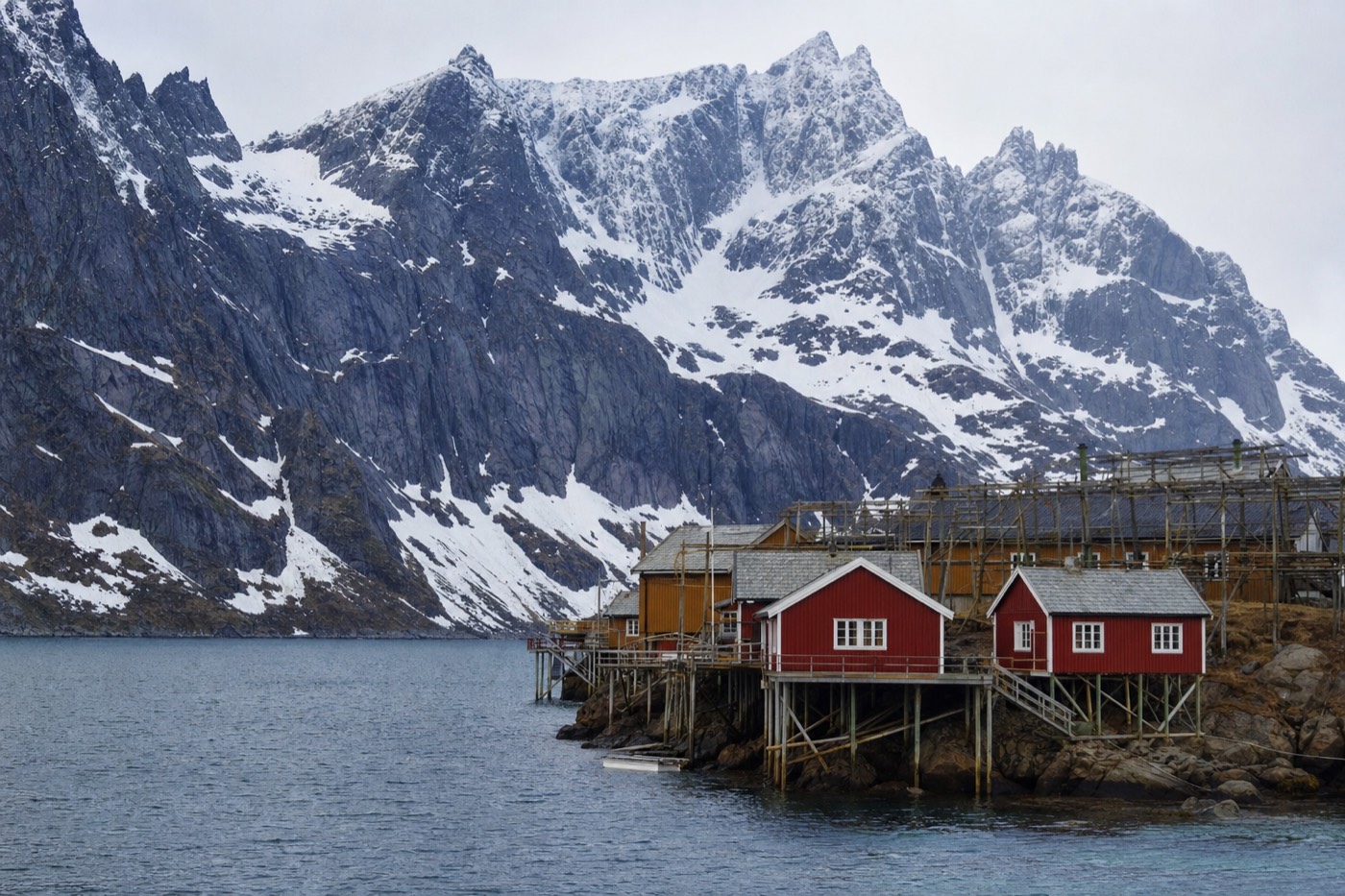 Traditional red fishermen's cabins over calm fjord water with peaks rising directly behind