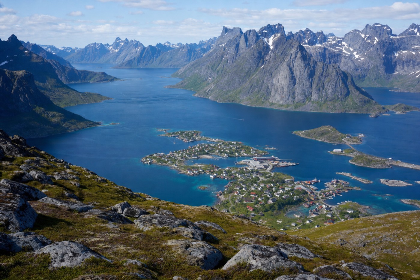 Panoramic view from a mountain summit over a scattered fishing village between jagged peaks